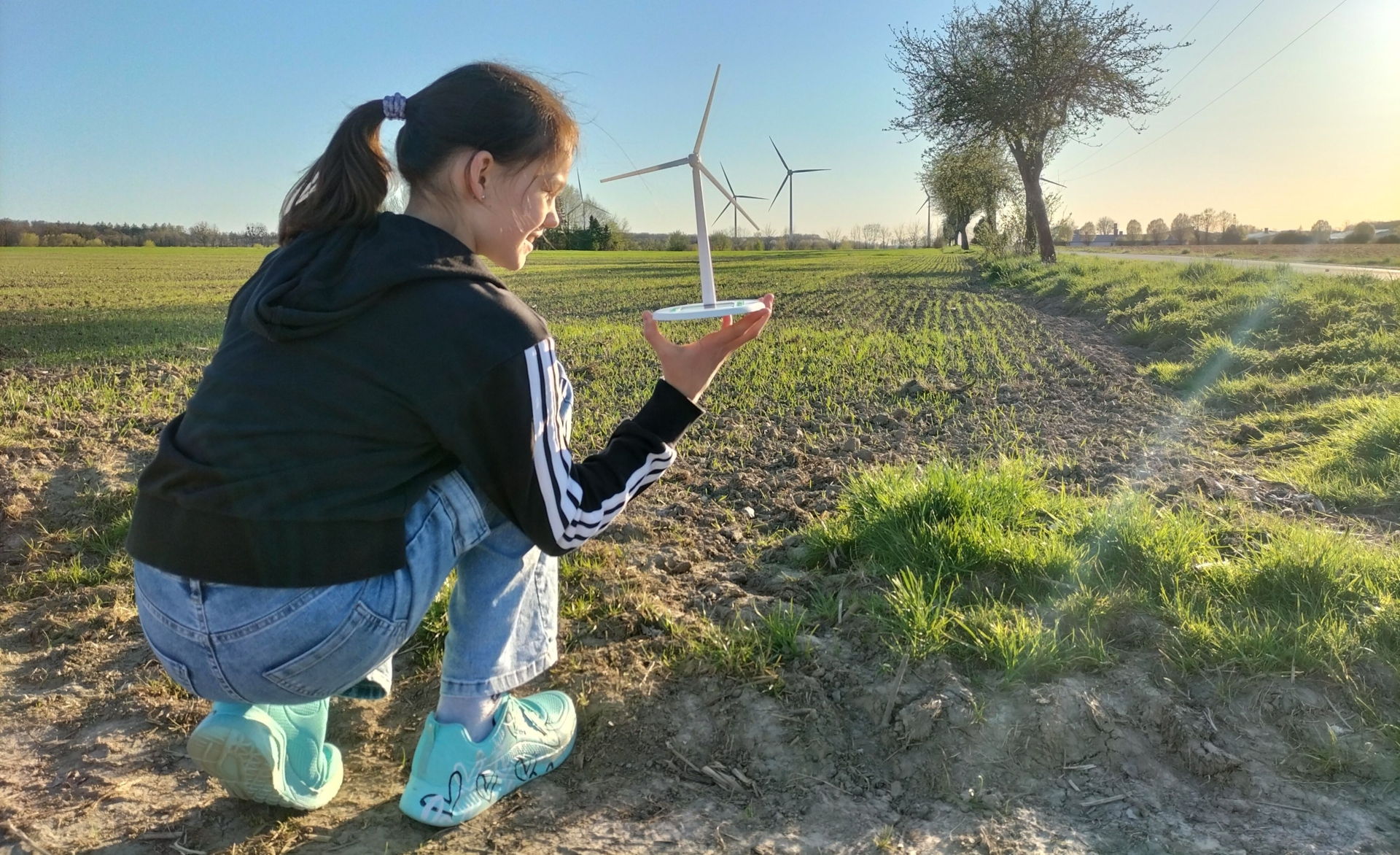 Mädchen hält ein Solar-Windrad in der Hand, im Hintergrund Windräder