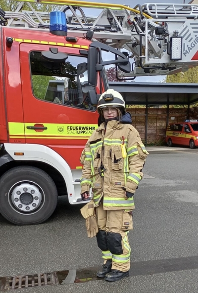 Mädchen in Feuerwehrschutzkleidung vor einem Feuerwehrauto.