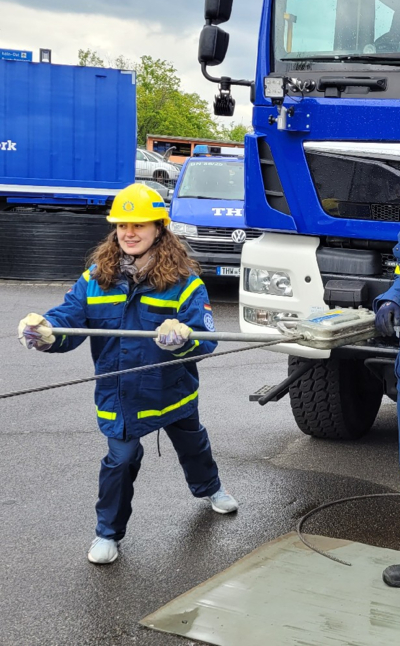Mädchen mit Arbeitskleidung und Schutzhelm bedient eine Winde an einem LKW.