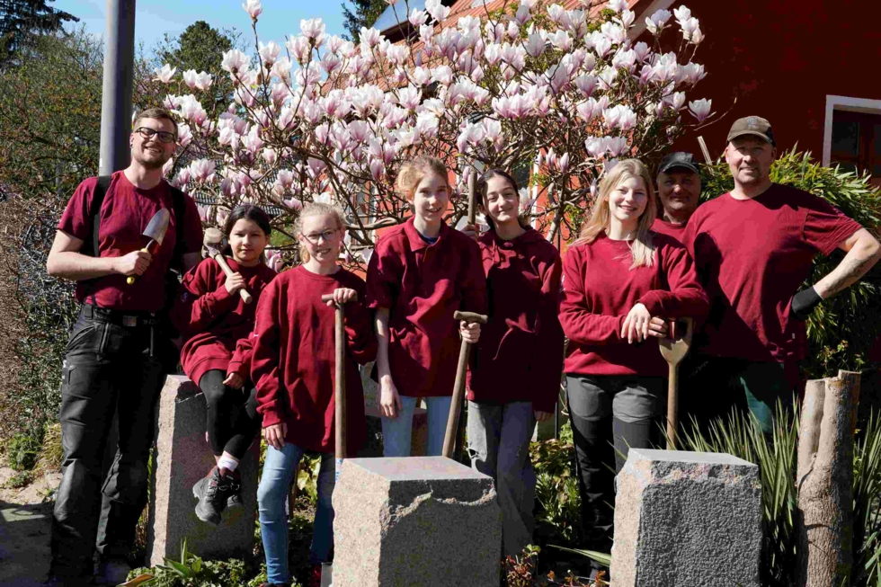 Girls'Day-Teilnehmerinnen in Arbeitskleidung mit Mitarbeitern vor Magnolienstrauch