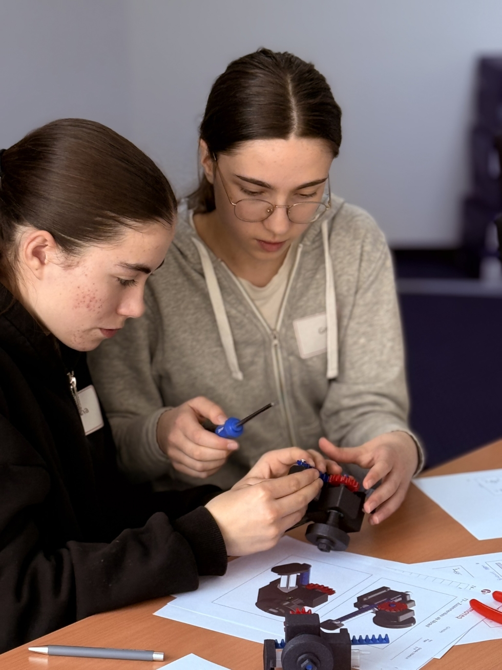 Zwei Girls' Day-Teilnehmerinnen arbeiten gemeinsam an einem technischen Modell mit Schraubendrehern und Bauanleitung auf einem Tisch