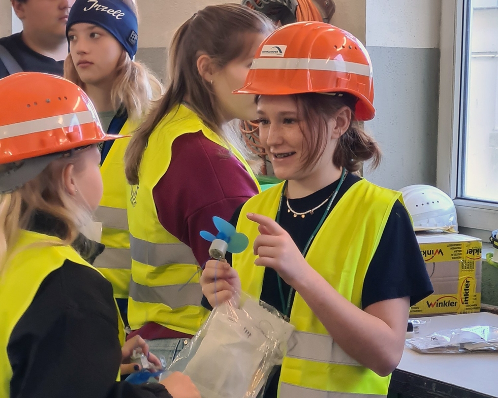 Girls' Day-Teilnehmerinnen in Sicherheitskleidung und Helmen, lächeln und unterhalten sich