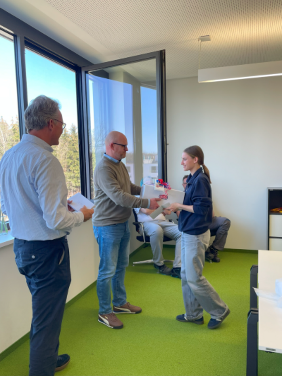 Girls' Day-Teilnehmerin erhält in einem Büro von einem Mitarbeiter ein Geschenk und eine Teilnahmebescheinigung