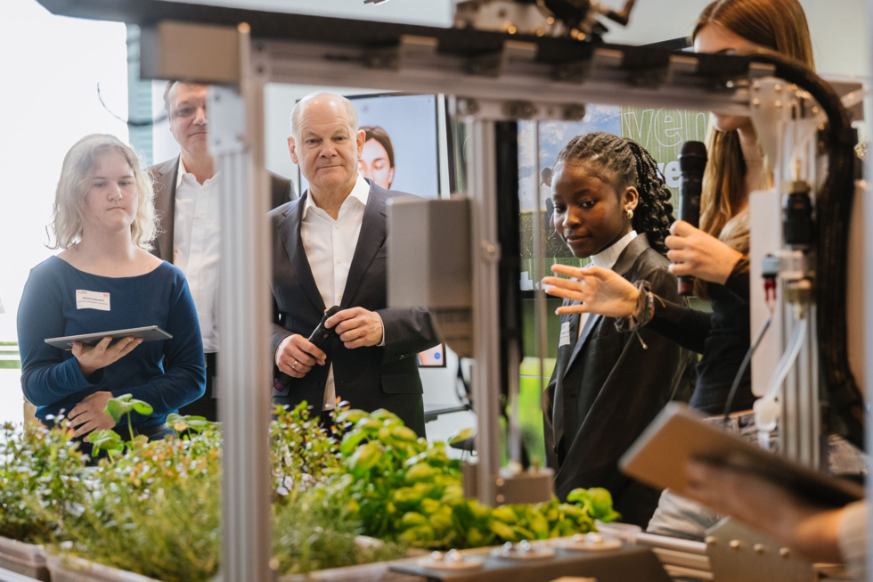 Schülerinnen mit Bundeskanzler Scholz hinter einem Tisch mit Grünpflanzen