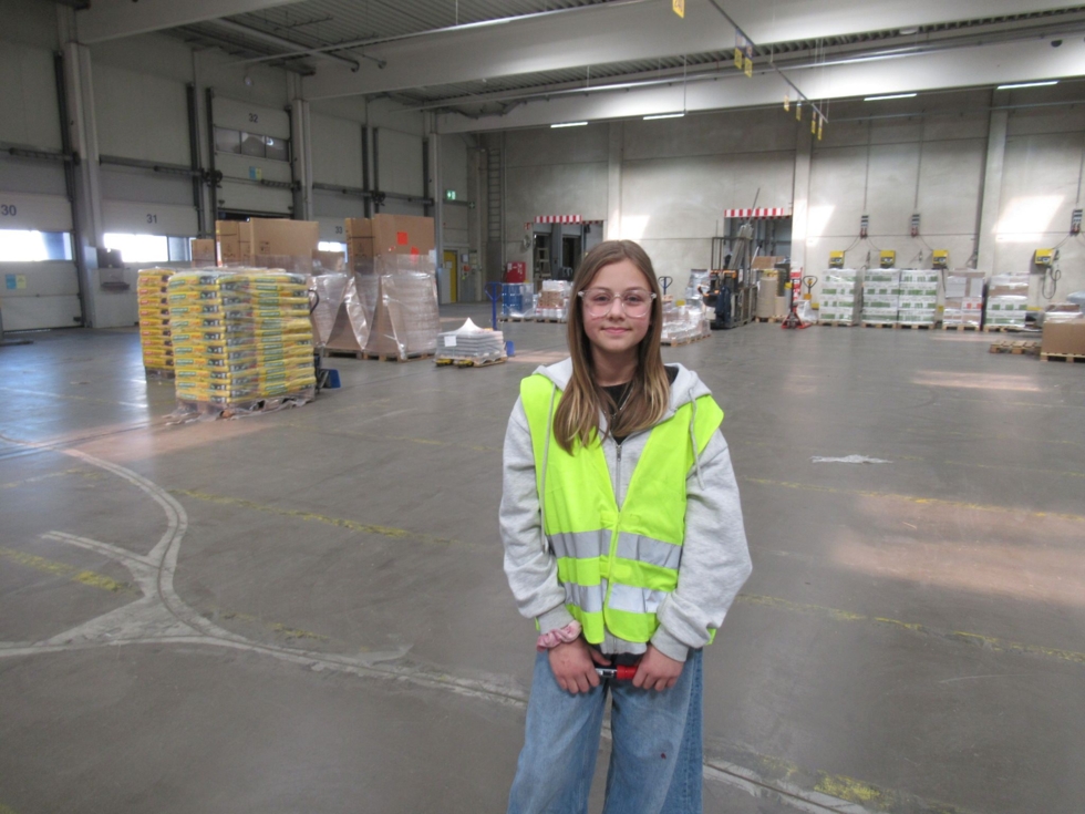 Girls'Day-Teilnehmerin steht in einer gelben Sicherheitsweste in einem Lager mit Paletten und Kisten im Hintergrund