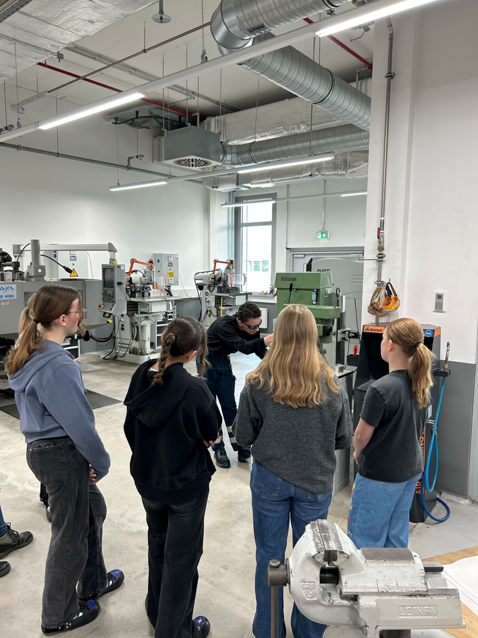 Girls' Day-Teilnehmerinnen beobachten einen Mitarbeiter, der eine Maschine in einer Werkstatt mit Metallbearbeitungsmaschinen bedient
