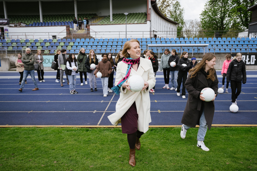 Im Vordergrund Ministerin mit Fußball in der Hand, im Hintergrund Schülerinnen mit Fußball