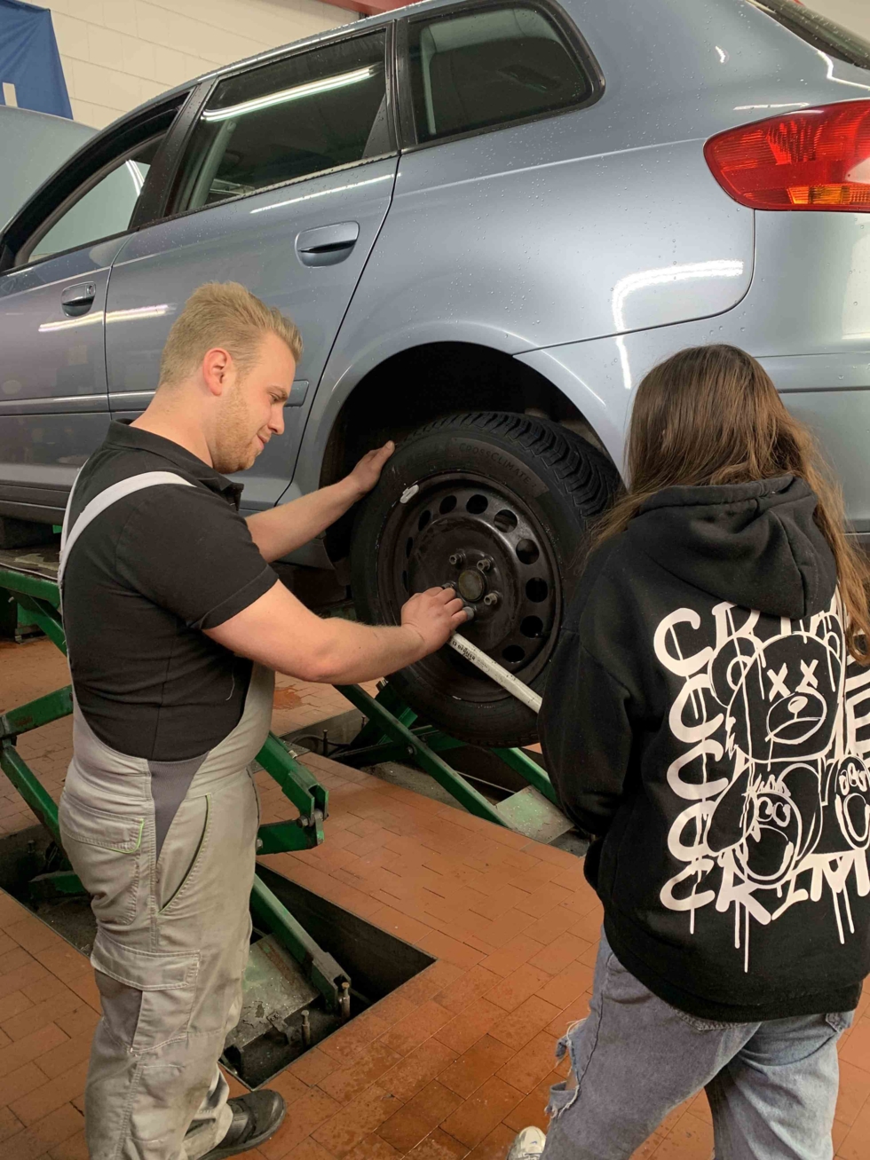 Girls'Day-Teilnehmerin und Mechaniker schrauben an einem Auto