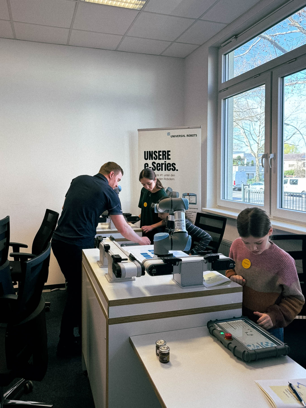 Ein Mitarbeiter und zwei Girls' Day-Teilnehmerinnen arbeiten an einem Tisch mit technischen Geräten in einem hellen Raum