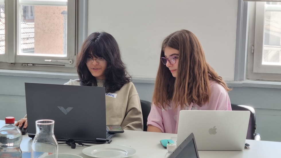 Zwei Girls' Day-Teilnehmerinnen sitzen nebeneinander an einem Tisch und arbeiten konzentriert an Laptops in einem hellen Raum mit großen Fenstern