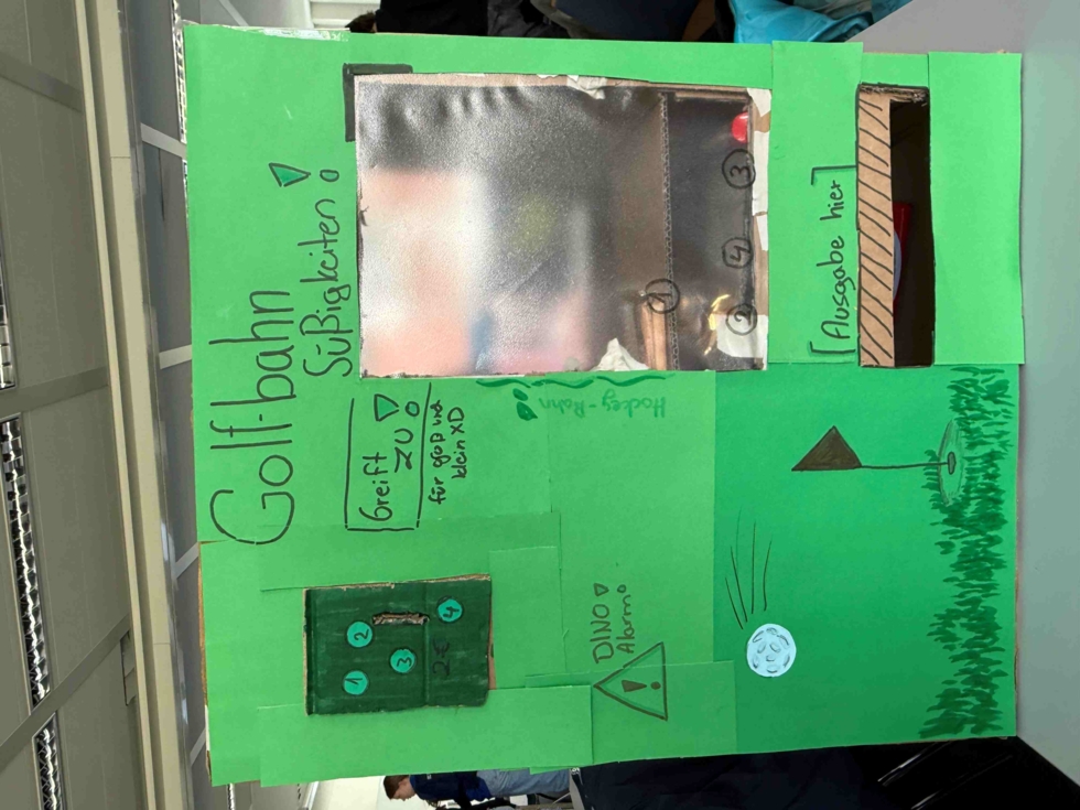 Grünes Plakat mit der Überschrift 'Golfbahn Süßigkeiten' und handgemalten Elementen wie einem Golfball, einem Loch mit Fahne und einem Bereich zur Ausgabe von Süßigkeiten