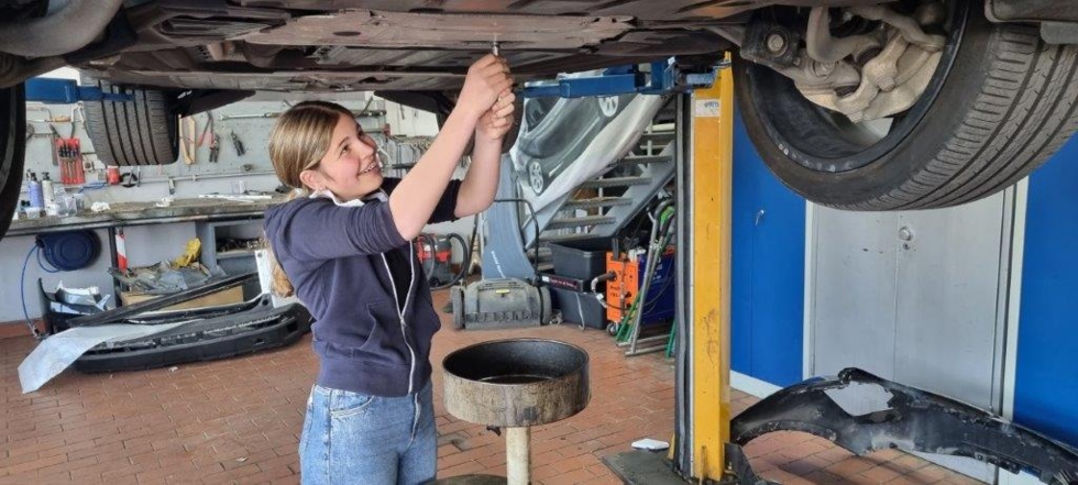 Mädchen steht unter einem Auto und schraubt etwas fest