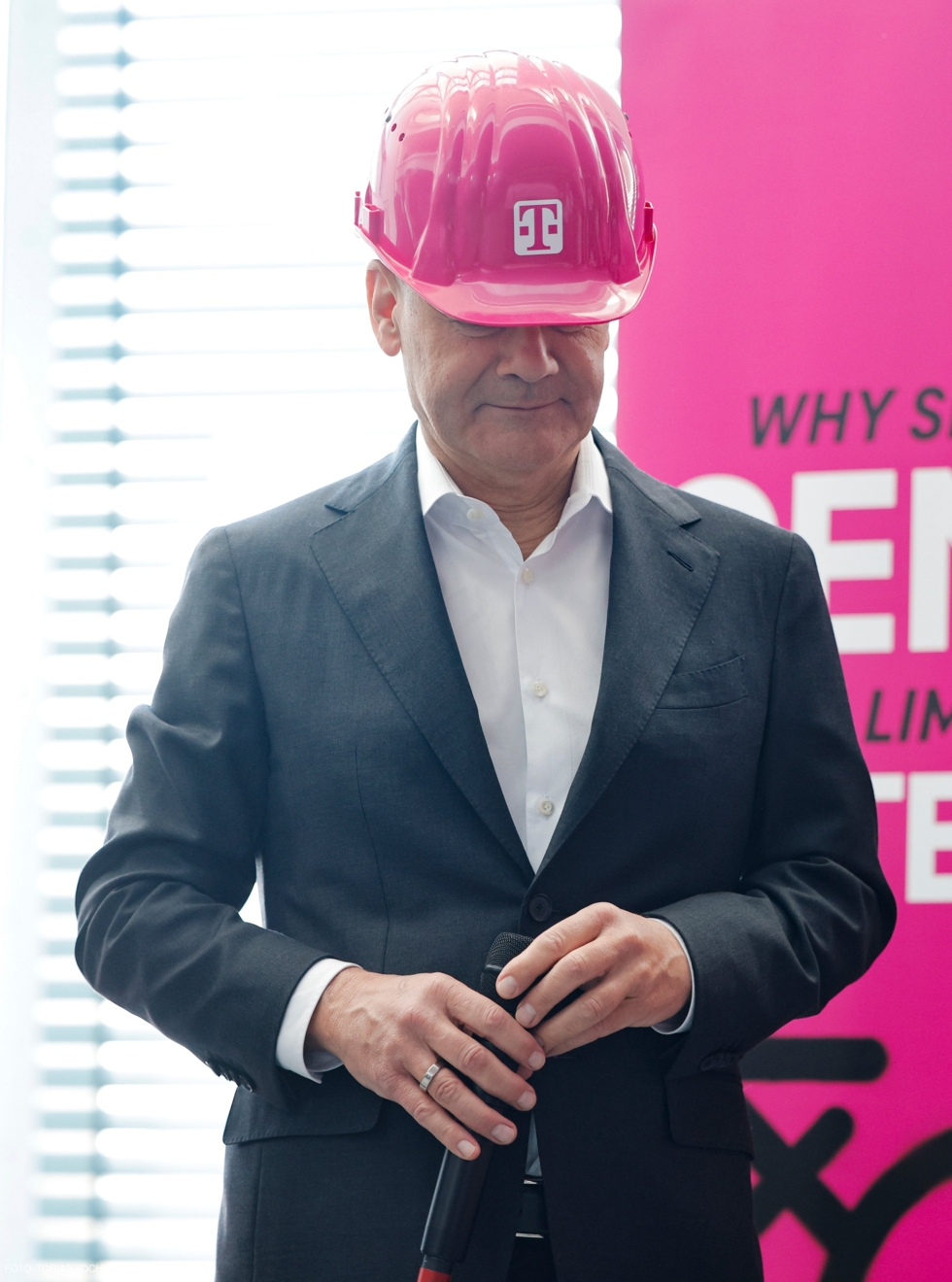 Bundeskanzler Olaf Scholz trägt einen magentafarbenen Schutzhelm mit dem Logo der Deutschen Telekom.
