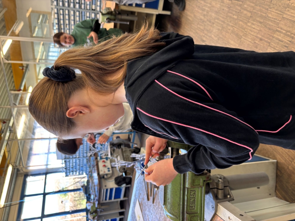 Girls' Day-Teilnehmerin arbeitet an einer Werkbank in einer Werkstatt mit Werkzeugen und Maschinen im Hintergrund