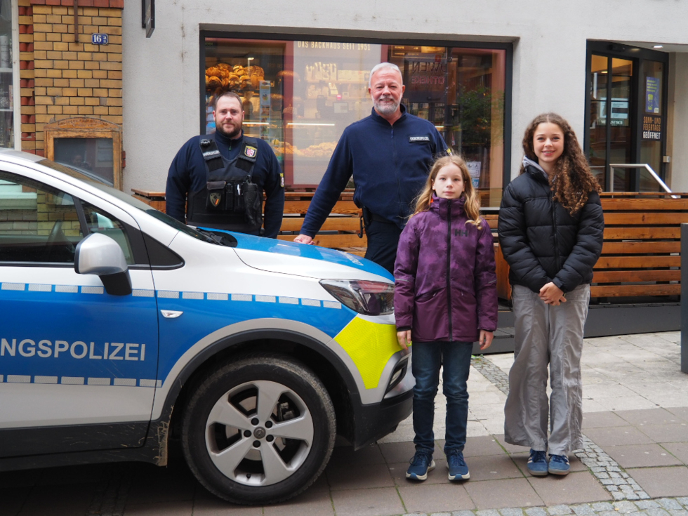 Girls'Day-Teilnehmerinnen mit Ordnungspolizisten vor Polizeiwagen