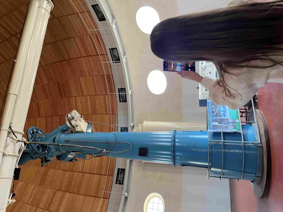 Girls' Day-Teilnehmerin fotografiert ein großes blaues Teleskop in einer Kuppel mit Holzdach