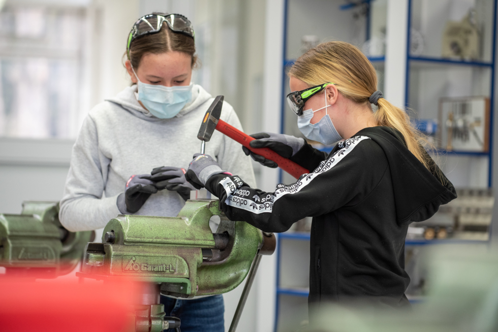 Zwei Mädchen mit Maske arbeiten am Schraubstock