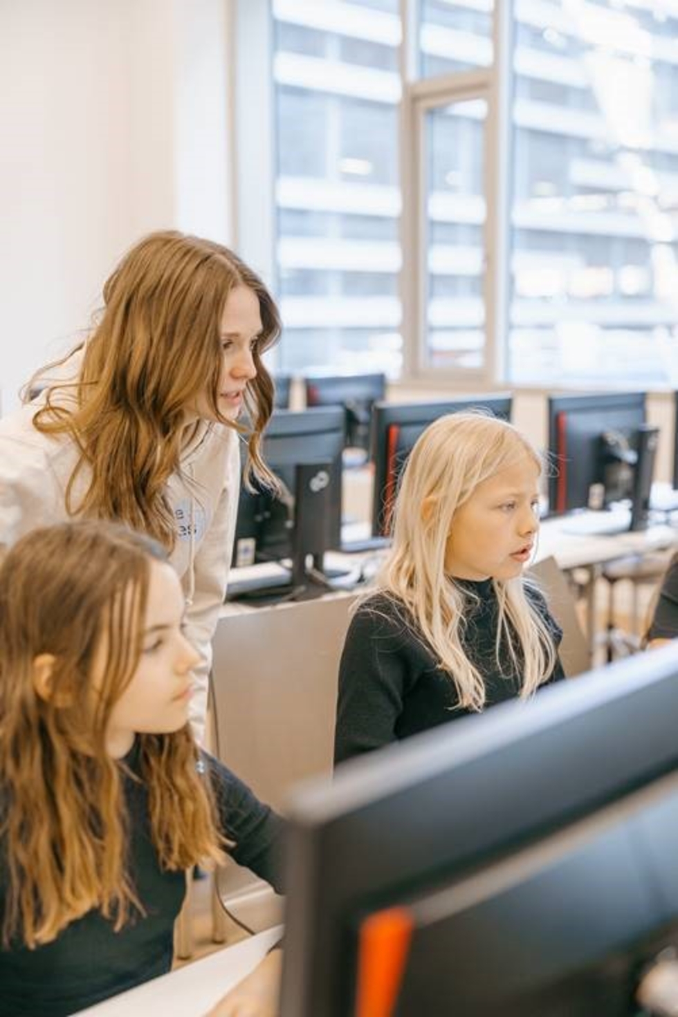 Drei Girls' Day-Teilnehmerinnen konzentrieren sich auf Computerbildschirme in einem modernen Büro mit großen Fenstern