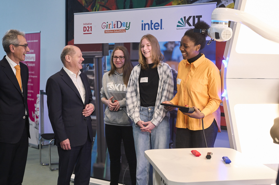 Hannes Schwaderer und Olaf Scholz mit Schülerinnen hinter einem Roboterarm.