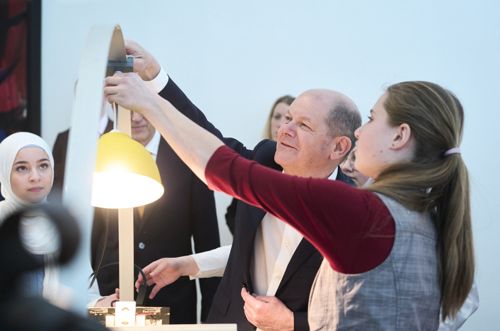 Bundeskanzler Olaf Scholz und eine Schülerin installieren eine Lampe.
