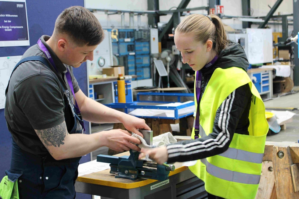 Girls'Day-Teilnehmerinnen in Werkstatt mit Mitarbeiter am Schraubstock