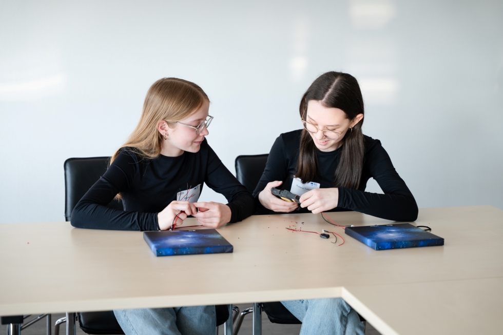 Zwei Girls' Day-Teilnehmerinnen sitzen an einem Tisch und arbeiten gemeinsam an einem Elektronikprojekt mit Kabeln und Bauteilen