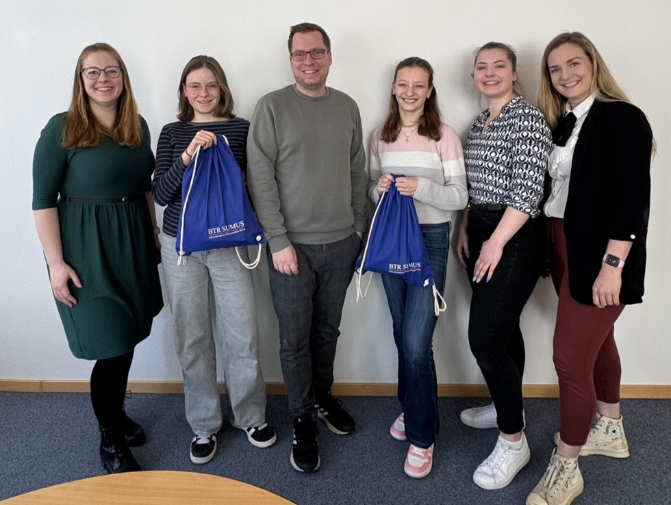 Girls' Day Teilnehmerinnen mit Fach- und Führungskräften in einer Steuerberatungs- und Wirtschaftsprüfungskanzlei, lächelnd in einem Besprechungsraum.