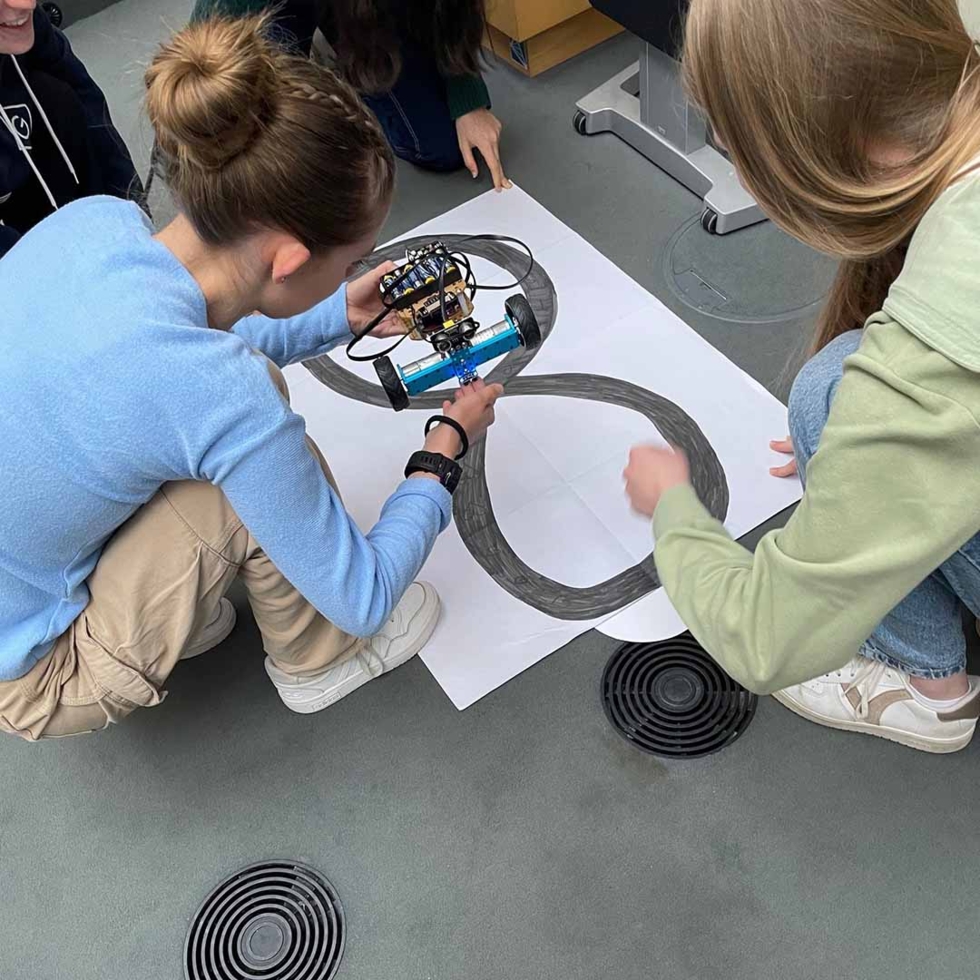 Girls'Day Teilnehmerin beim ausprobieren eines kleinen Roboters, welcher Linien auf ein Papier malen kann