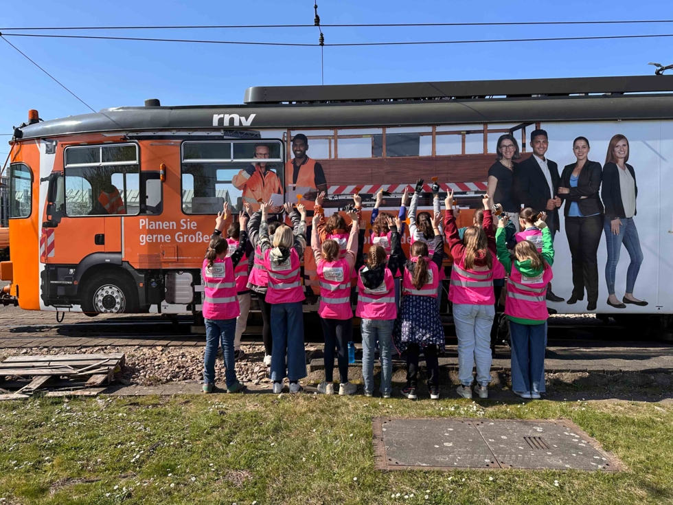 Girls'Day-Teilnehmerinnen mit Warnwesten von hinten fotografiert vor einem Schienenbauwagen