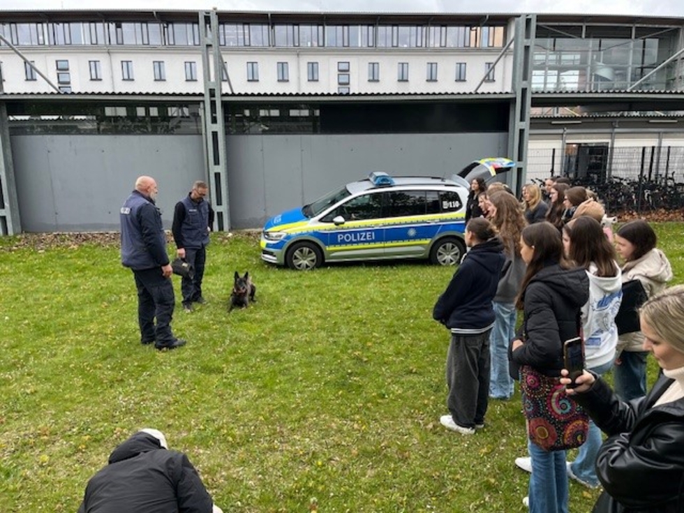 Girls'Day-Teilnehmerinnen mit Polizisten neben Polizeiauto und Polizeihund